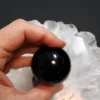 Esfera obsidiana negra natural com 5 cm de diâmetro exibida na mão.